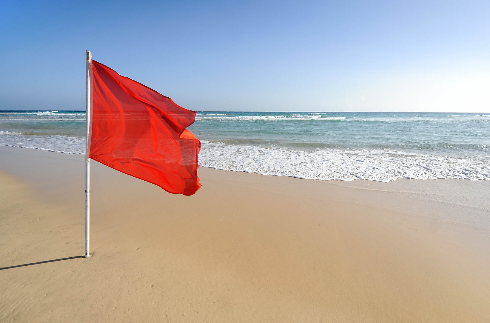 A warning sign of a red flag at a beautiful beach with a blue sky and a turquoise sea